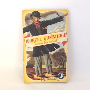 Puede incluir: Libro de bolsillo vintage "Worzel Gummidge" de Barbara Euphan Todd. La portada presenta una ilustración de un espantapájaros con abrigo y sombrero negros, con bufanda roja y un pájaro. Un libro de Puffin Story.