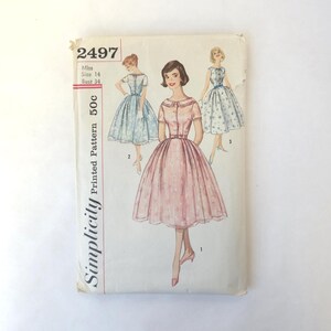 May include: Vintage Simplicity printed sewing pattern, number 2497, featuring illustrations of three different dresses. The pattern includes a size 14 with a 34-inch bust. The cover has a pink and white floral dress design.