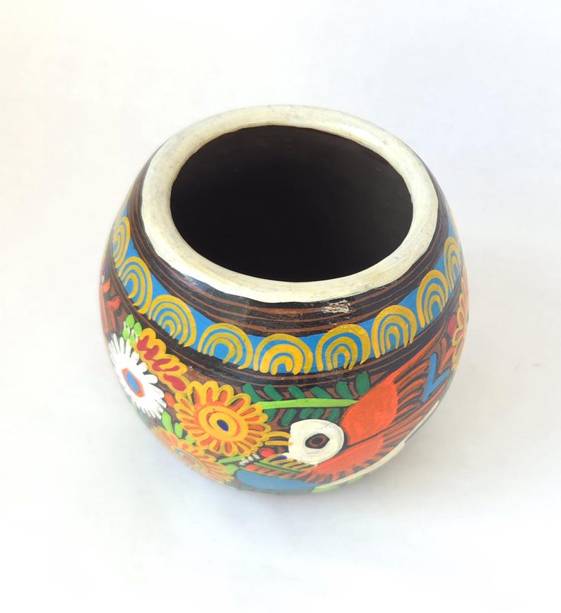 May include: A hand-painted, round ceramic vase with a wide opening. The vase features a brown base with colorful floral and bird designs in orange, yellow, blue, and white. The rim is white.