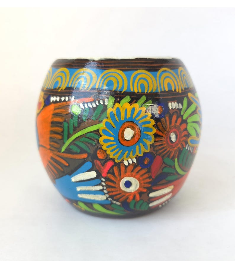 May include: A hand-painted, round, dark brown container with a white rim. The container is decorated with colorful floral and abstract designs in orange, blue, green, and red. The design includes a blue and yellow pattern around the top.