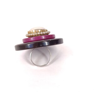 May include: A black, pink, and white button ring with a pearl accent.