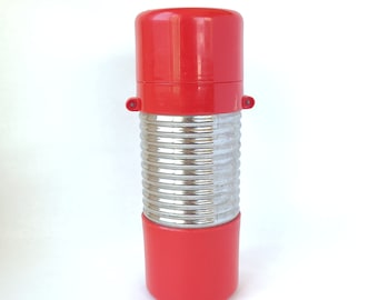 May include: A red and silver thermos with a ribbed body and a red lid. The thermos is isolated on a white background.