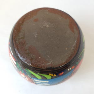 May include: A hand-painted ceramic vase with a dark brown base and a black exterior. The vase features colorful floral and geometric designs in red, blue, green, and white. The vase is round and has a smooth finish.