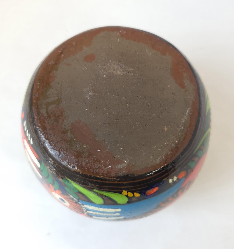 May include: A hand-painted ceramic vase with a dark brown base and a black exterior. The vase features colorful floral and geometric designs in red, blue, green, and white. The vase is round and has a smooth finish.