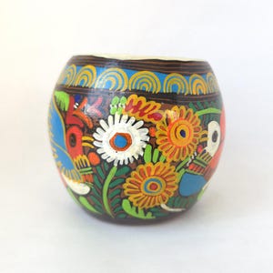 May include: A hand-painted, round, brown vessel with a wide opening. The vessel is adorned with colorful floral and bird designs in shades of red, yellow, blue, and green. The rim is painted with a blue and yellow pattern.