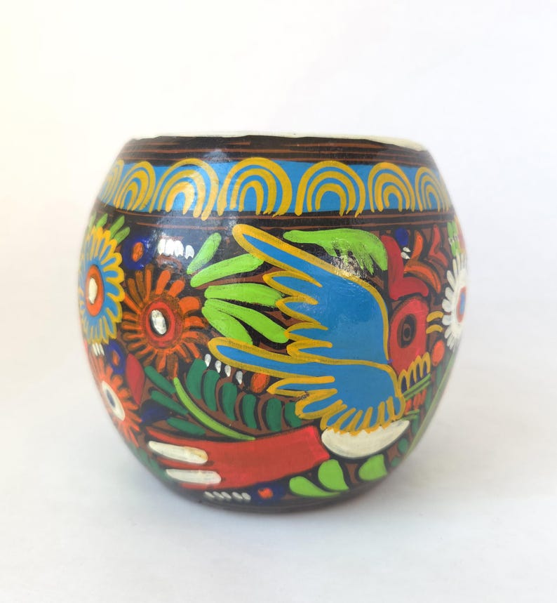 May include: A hand-painted, round wooden container with a dark brown base. The container is adorned with colorful floral and bird designs in blue, green, red, orange, and white. The rim features a blue and yellow arched pattern.