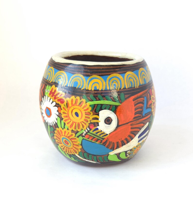 May include: A hand-painted ceramic vase with a brown base, adorned with a vibrant design. The artwork features a red bird, yellow and white flowers, and blue accents. The rim is white, and the vase has a rounded shape.