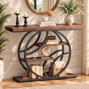 May include: A rectangular console table with a dark wood grain finish and a black metal frame featuring two large intersecting circular supports. The table includes two interior shelves holding books, a decorative shell, and a small digital clock.