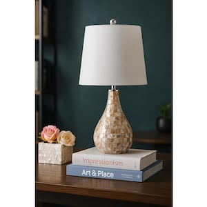 May include: A decorative table lamp with a white lampshade and a mosaic-patterned base. The lamp sits on a dark wooden surface, next to a small box with roses and two books titled "Impressionism" and "Art & Place".