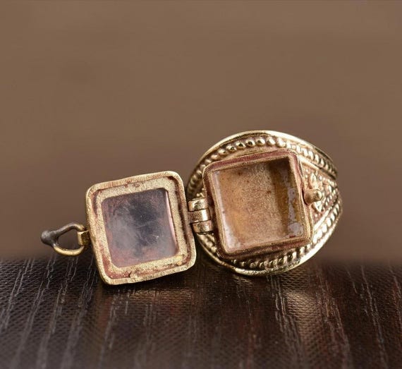 A handmade brass ring with a hinged secret compartment lid — the centuries-old 'poison ring' concept executed in gemstone and brass by an actual artisan at a price that signals serious craft.