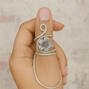 Könnte beinhalten: Ein silberner Ring mit floralem Design. Der Ring umschließt einen Finger, mit einer Spirale und einer Blume in der Mitte. Ein einzigartiges Schmuckstück.