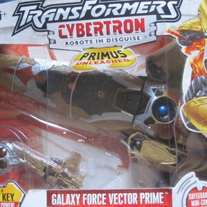 May include: A gold and silver Transformers Cybertron Galaxy Force Vector Prime action figure in a plastic package. The figure is in robot mode and has a blue eye. The packaging features the Transformers logo, the Cybertron logo, and the Primus Unleashed logo. The text "Cyber Planet Key Unlock the Power" and "Safeguard Mini-Con" is also visible on the packaging.