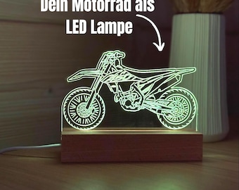 Könnte beinhalten: Eine LED-Lampe aus klarem Acryl mit der gravierten Kontur eines Motocross-Motorrads, das in hellem Grün leuchtet. Das Acrylelement ist auf einem rechteckigen Holzsockel montiert, von dem ein weißes Stromkabel seitlich wegführt.