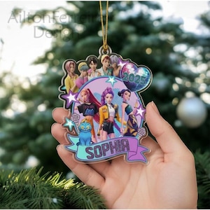 A hand holding a colorful ornament featuring a group of cartoon characters, including a girl named Sophia, against a blurred background of a Christmas tree.