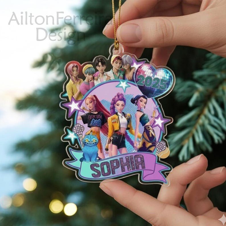 A hand holding a colorful ornament featuring a group of cartoon characters, including a girl named Sophia, against a blurred background of a Christmas tree.