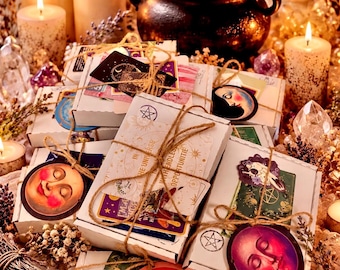 May include: A collection of white rectangular boxes tied with twine, decorated with celestial and moon-themed stickers. The boxes are surrounded by lit pillar candles, crystals, and a steaming black cauldron, creating a mystical atmosphere.