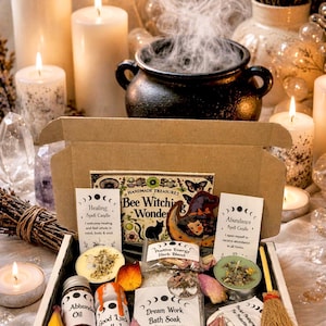 May include: A witch-themed gift box with candles, a cauldron, and various spell components. The box includes jars, bath soaks, herbs, and a small broom. The text on the box reads "Bee Witching Wonder".