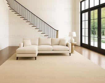 May include: A beige sectional sofa with a matching rug in a modern living room setting. The room features a staircase with black railings and a large window with black frames. A side table with a lamp is next to the sofa.