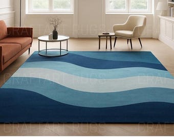 May include: A large rectangular area rug with a wavy pattern in shades of blue and white. The rug's design features broad, horizontal stripes of varying blue tones, creating a flowing, ocean-like aesthetic. The rug is placed on a light-colored wooden floor.