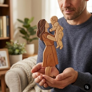 Puede incluir: Una figura de madera que representa a una persona con cabello largo y oscuro que lleva un vestido, sosteniendo a un niño pequeño en el aire. La escultura está hecha de diferentes tonos de madera natural, con piezas lisas y entrelazadas.