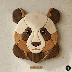 Pode incluir: Arte de parede de urso panda em madeira. O rosto do panda é feito de várias tonalidades de madeira, incluindo bege claro, castanho médio e castanho escuro. Os olhos são castanhos escuros com um acabamento brilhante, e o nariz é de um tom mais escuro. O texto "MADE BY LOVE" está numa pequena placa de madeira.