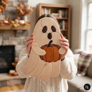 May include: A wooden puzzle shaped like a ghost holding a pumpkin. The ghost is made of light-colored wood with dark wood eyes and mouth. The pumpkin is crafted from orange-toned wood with a dark brown stem. The pieces fit together seamlessly.
