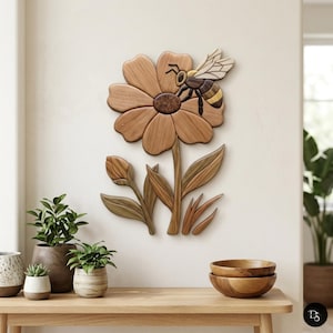 May include: Wooden wall art featuring a large flower with a bee. The flower has multiple petals and a dark brown center. The bee is detailed with black and yellow stripes. The art piece is mounted on a white wall.