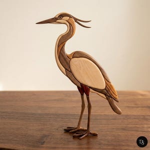 May include: A wooden heron sculpture, featuring a long neck and legs. The bird is made from various wood tones, including light beige, medium brown, and dark brown. The sculpture has a detailed beak and a crest on its head, and is standing on a wooden surface.