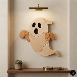 May include: A wall-mounted wooden ghost decoration featuring light and medium-toned wood segments. The ghost has two oval eyes and an oval mouth with dark cutouts. Below it, a small succulent in a pot and a magnifying glass sit on a shelf.