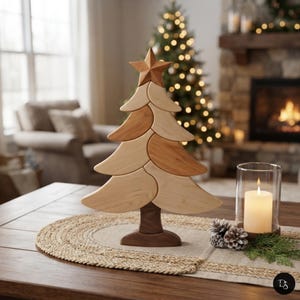 Peut inclure: Une sculpture décorative de sapin de Noël en bois composée de segments de bois clair et moyen imbriqués, surmontée d'une étoile à cinq branches. L'arbre repose sur une base brun foncé, avec des branches courbes lisses et un grain naturel.