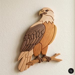 May include: A wall-mounted wooden eagle sculpture crafted from various wood tones including light tan, medium brown, and dark brown. The eagle is depicted in profile, perched on a branch, with layered wooden pieces creating the wing feathers.
