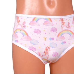 May include: White underwear featuring a repeating pattern of unicorns, rainbows, clouds, and crowns. The underwear has a white trim and a light pink background. The unicorns have pink manes and tails.
