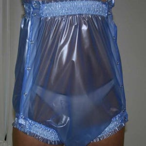 May include: Light blue plastic waterproof pants with elastic waist and leg openings. The pants have snap closures along the sides and a gathered ruffle detail at the waist and leg openings. The material is shiny and translucent.