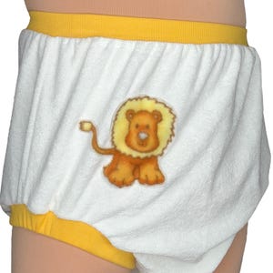 Puede incluir: Braguita de pañal de rizo blanco con ribete amarillo. Un aplique de león de dibujos animados está centrado en la parte delantera. El león es marrón y amarillo con una expresión amigable. La braguita tiene cintura y aberturas de piernas elásticas.
