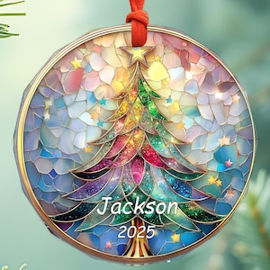 May include: A round Christmas ornament with a colorful stained-glass design. The ornament features a Christmas tree with the name "Jackson" and the year "2025". It hangs from a red ribbon. The ornament has a gold-colored border and is decorated with stars.