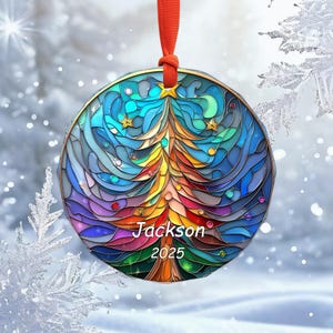 May include: A round Christmas ornament with a stained-glass design. The ornament features a colorful Christmas tree in the center, with the name "Jackson" and the year "2025" below. The ornament is trimmed in gold and has a red ribbon for hanging.