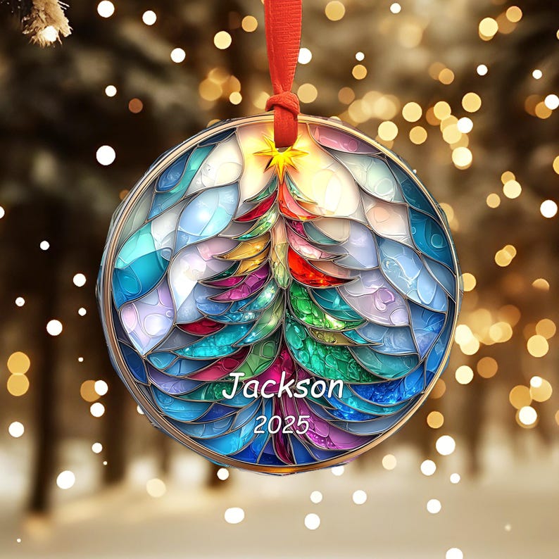 May include: A round Christmas ornament with a colorful stained-glass design of a Christmas tree. The ornament has the name "Jackson" and the year "2025" printed on it. It is suspended by a red ribbon.