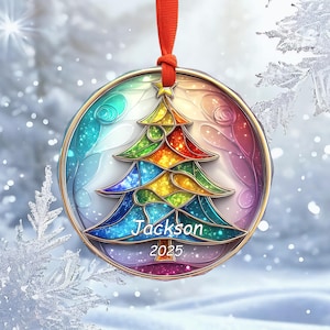 May include: A round Christmas ornament with a colorful stained-glass design of a Christmas tree. The ornament has a gold-colored border and a red ribbon for hanging. The name "Jackson" and the year "2025" are printed on the ornament.