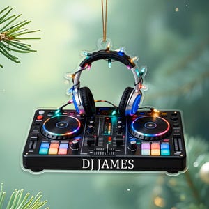 May include: A DJ-themed Christmas ornament featuring a black DJ mixer with colorful lights and two turntables. A pair of headphones is adorned with string lights. The ornament has the text "DJ JAMES" on the mixer.