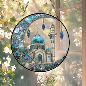 May include: A stained glass crescent moon with a mosque design. The mosque features a blue dome and minaret, with hanging blue crystal-like ornaments. The artwork is framed in black and hangs from a chain.