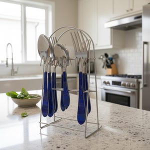 May include: A set of stainless steel cutlery with blue handles is displayed in a wire rack. The set includes spoons, forks, and knives. The rack is on a kitchen countertop. A bowl of basil is in the background.