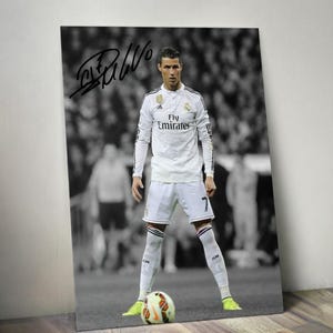 May include: Black and white photograph of a soccer player in a white jersey with the text "Fly Emirates" and the number 7. The player is standing on a soccer field with a soccer ball at his feet. The image is signed.