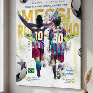 Könnte beinhalten: Gerahmter Leinwanddruck mit Ronaldinho und Lionel Messi in ihren Trikots der Fußballnationalmannschaft. Der Druck enthält den Text "MESSI RONALDINHO" in goldfarbenen Buchstaben sowie ihre Geburtsjahre und -orte. Der Hintergrund hat ein weißes und gelbes abstraktes Design.