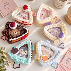 May include: Six triangular plush pouches shaped like cake slices, each featuring a clear window displaying a small stuffed animal character. The pouches are decorated with ruffled edges and plush toppings like cherries, strawberries, and stars, and include heart-shaped zipper pulls.
