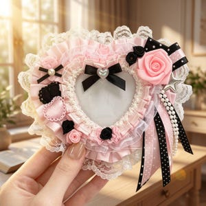 May include: A heart-shaped photo frame decorated with pink ruffled fabric, white lace trim, and black ribbons. It features small black and pink fabric roses, a central black bow with a heart charm, and a dangling strand of white faux pearls.