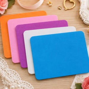 Puede incluir: Un conjunto de cinco láminas de espuma rectangulares en colores naranja, rosa, morado, blanco y azul. Cada lámina tiene una superficie mate lisa y esquinas redondeadas. Las láminas están apiladas de forma escalonada, mostrando sus colores sólidos.