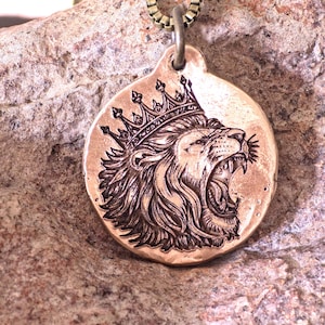 Peut inclure: Un pendentif circulaire de couleur bronze orné d'une gravure représentant un lion rugissant portant une couronne. Le pendentif présente un bord texturé et irrégulier, suspendu à une chaîne en métal, mettant en valeur les détails de la crinière.