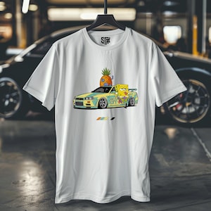 May include: White t-shirt featuring a cartoon graphic of SpongeBob SquarePants leaning on a yellow and blue car with a pineapple on top. The shirt has a black hanger and the STX logo.