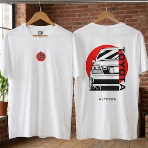 May include: White t-shirts with a front and back design. The front features a small red logo. The back displays a car graphic with the word "TOYOTA" in red and "ALTEZZA" in black.