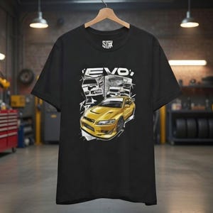 May include: Black t-shirt featuring a yellow sports car graphic with the word "EVO" in white. The shirt is hanging on a wooden hanger in a garage setting. The STX logo is visible on the upper left.